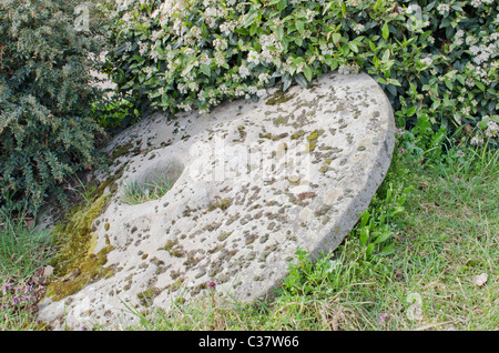 Old mill stone lying amongst shrubs  in the town of Diss, East Anglia, England, UK Stock Photo