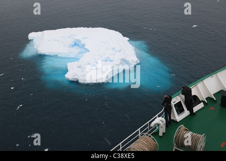 Two passengers on polar cruise vessel looking at small glacial iceberg in [Lemaire Channel], [Antarctic Peninsula] Stock Photo