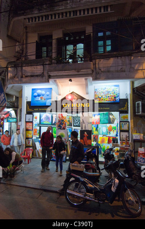 Vertical night time view of a tourists outside a gallery selling big paintings on Hang Be street in the Old Quarter in Hanoi. Stock Photo