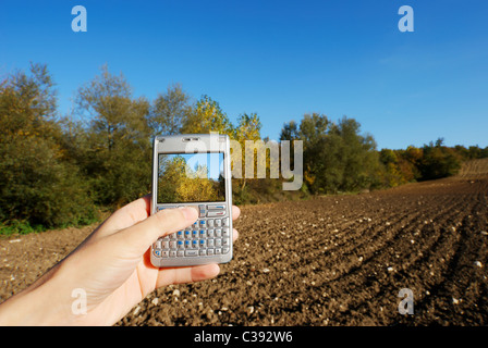 Cellphone in hand and bright autumnal rural landscape Stock Photo