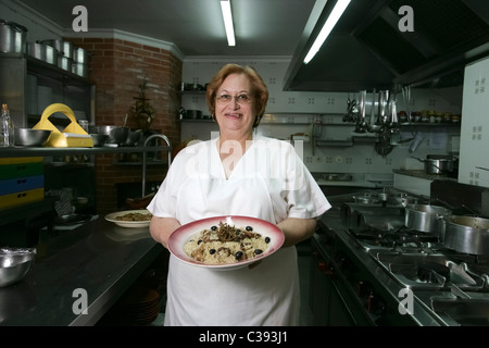 Woman chef holding plate with food in a restaurant's modern professional kitchen Stock Photo