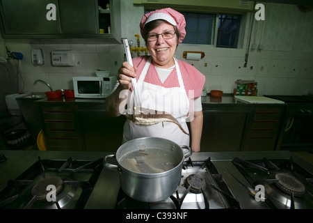 Portrait of woman chef holding fish over a pan in a restaurant's modern professional kitchen Stock Photo