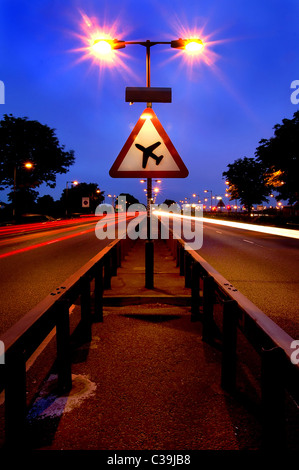 A long exposure of a dual carriageway close to Heathrow Airport and a road sign warning of low flying aircraft. Stock Photo