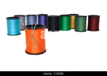 Colorful spools of thread with an orange one holding needles in the foreground. Stock Photo