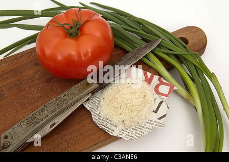 Tomato, salt on the newspaper, old knife and onions on a board Stock Photo