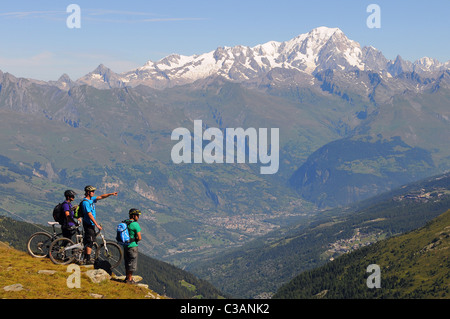 Three mountain bikers look across the valley from the La Plagne ski resort to Mont Blanc and the town of Bourg-Saint-Maurice Stock Photo