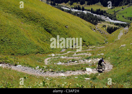 A mountain biker rides down a winding path high above the village of Champagny in the French Alps. Stock Photo