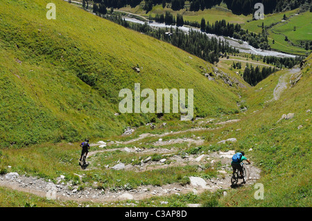 Two mountain bikers ride down a winding path high above the village of Champagny in the French Alps. Stock Photo