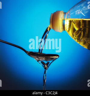 pouring olive oil on spoon, blue background Stock Photo