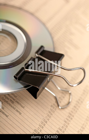 Close photo of paperclip attached to disk laying on financial newspaper. Stock Photo