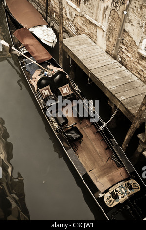 A traditional flat-bottomed Gondola (Venetian rowing boat) tied to a dock in a small canal of Venice, Italy. Stock Photo