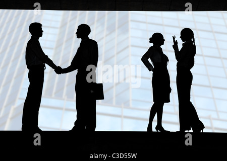 Businessmen congratulating each other with successful deal while two ladies talking behind Stock Photo
