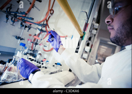 Close up of male scientist wearing white lab coat goggles and purple gloves working at fume cupboard with pipette and flasks Stock Photo