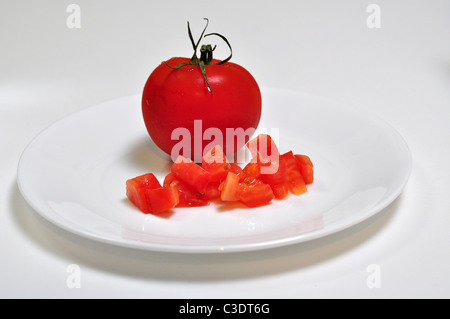 A bright red whole tomateo sits on a white background with a diced tomatoe. Stock Photo
