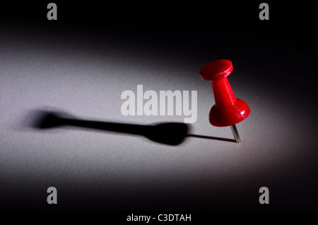 Red push pin under a spotlight with long shadow casted Stock Photo