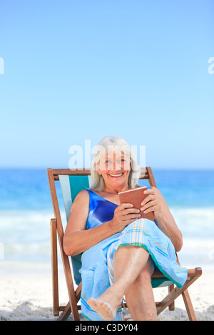 Senior woman reading a book on the beach Stock Photo