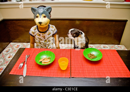Child in wolf mask at table with pet dog Stock Photo