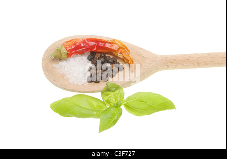 Chilli pepper, salt and pepper in a wooden spoon with fresh basil leaves on white Stock Photo