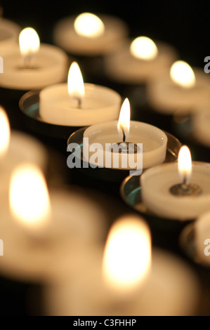 Three rows of burning votive candles with a black background Stock Photo