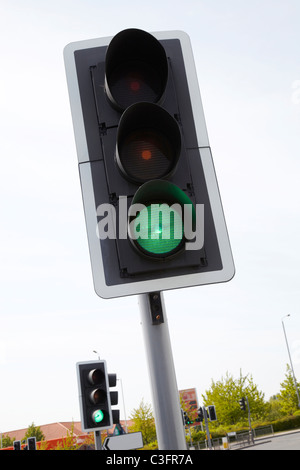 Traffic Light showing green in UK. Traffic light shot from below against bright blue sky. The green light signifies Go Stock Photo