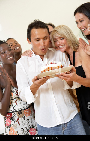 Friends watching woman blow out birthday cupcake in restaurant Stock