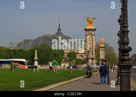 Parisians and tourists enjoy spring weather on a Sunday afternoon in Paris. Young men play football near Pont Alexandre III. Stock Photo