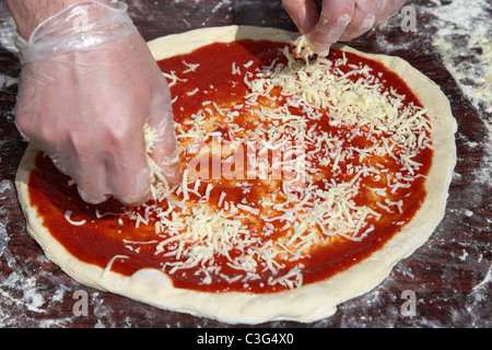spreading cheese over tomato sauce and pizza dough base to make fresh pizza Stock Photo