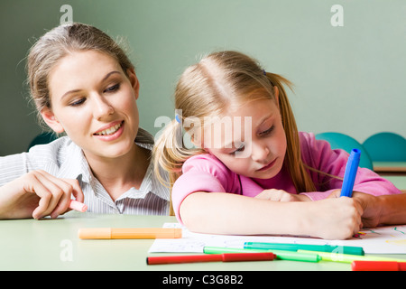 Portrait of diligent girl drawing something under tending of her teacher Stock Photo