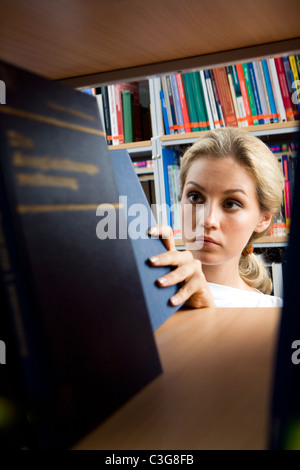 Image of young girl searching for necessary book on bookshelf in library