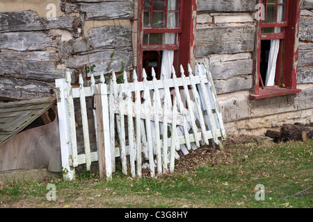 Old white picket fence leaning against an old cabin wall Stock Photo