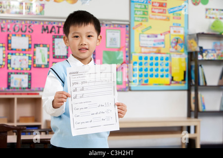 Young boy proudly holding up his work in class Stock Photo