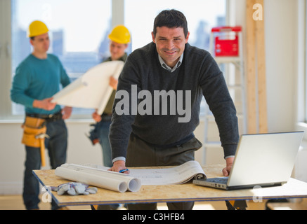 Architect preparing blueprint, construction workers in background Stock Photo