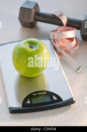 Green apple on weight scale, tape measure and exercise weight in background Stock Photo