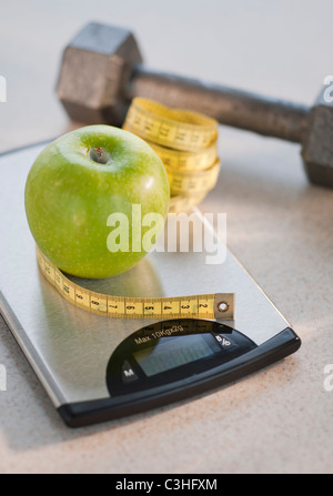 Green apple on weight scale, tape measure and exercise weight in background Stock Photo