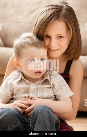 Portrait of Girl (10-11) with brother (2-3) sitting on floor Stock Photo