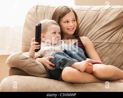 Girl (10-11) with brother (2-3) sitting on sofa, watching TV Stock Photo