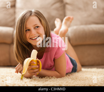 Girl (10-11) lying on rug, eating banana Stock Photo