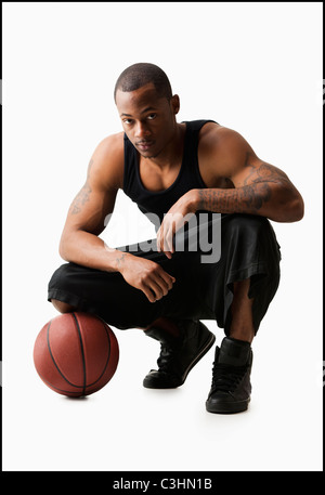 Studio shot of man with basketball crouching Stock Photo