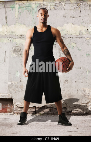 Portrait of young man with basketball against dilapidated wall Stock Photo
