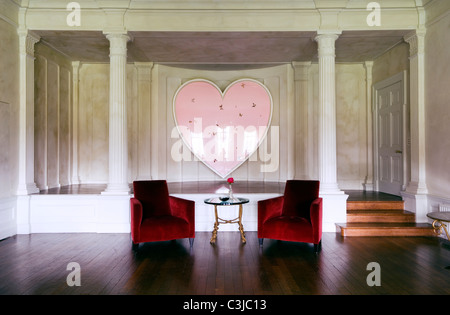 Red velvet armchairs in wooden living space with Damian Hirst heart shaped artwork in background Stock Photo