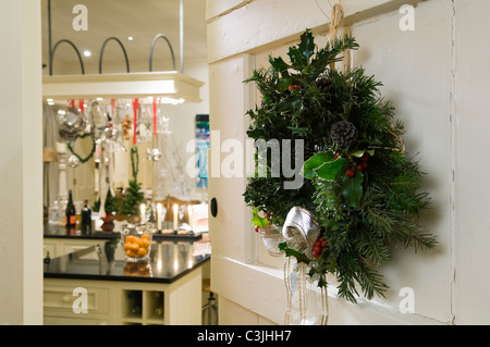 Christmas wreath on white open door with view through to kitchen with festive decorations Stock Photo