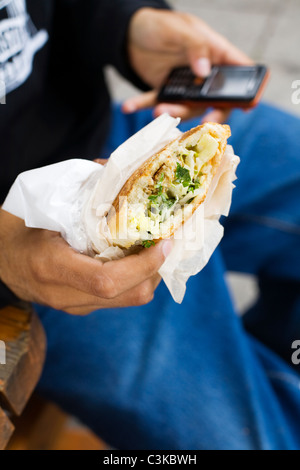 Close up of boys hands holding falafel and mobile phone Stock Photo