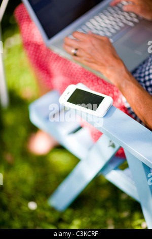Women using laptop, focus on mobile phone on chair Stock Photo