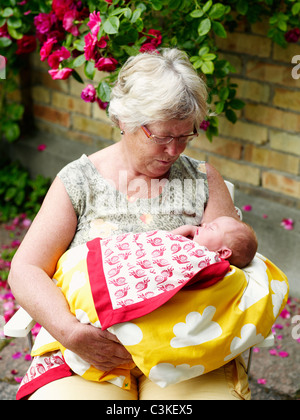 Grandmother sitting in front of house and holding baby Stock Photo