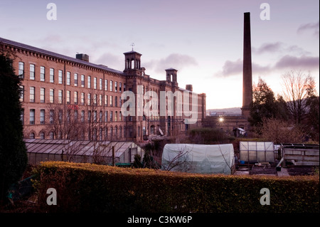 Salts Mill (chimney & historic Victorian textile factory building & greenhouses in Saltaire village allotments) at sunrise - Yorkshire, England, UK.