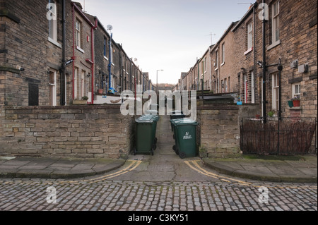 Narrow back street off Albert Terrace, Saltaire village (2 rows of terraced houses, green wheelie bins lined-up, stone setts) - Yorkshire, England, UK Stock Photo