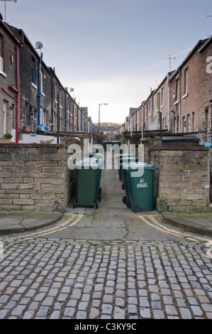 Narrow back street off Albert Terrace, Saltaire village (2 rows of terraced houses, green wheelie bins lined-up, stone setts) - Yorkshire, England, UK Stock Photo