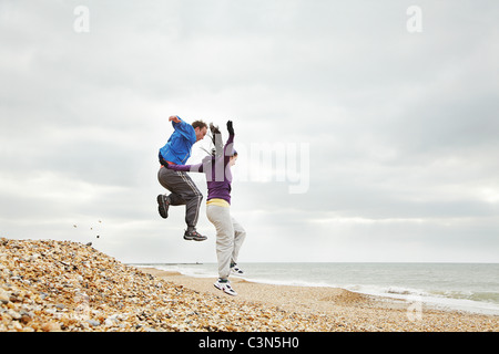 Couple jumping on beach on cloudy day Stock Photo