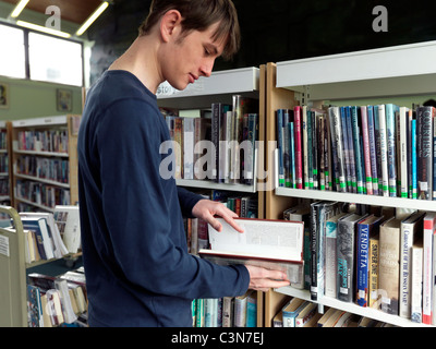 Teenage Boy Standing In A Library Looking At A Book Stock Photo