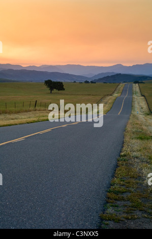 Golden sunrise light over long straight two lane country road and rolling hills in Spring, Santa Ynez Valley, California  Stock Photo